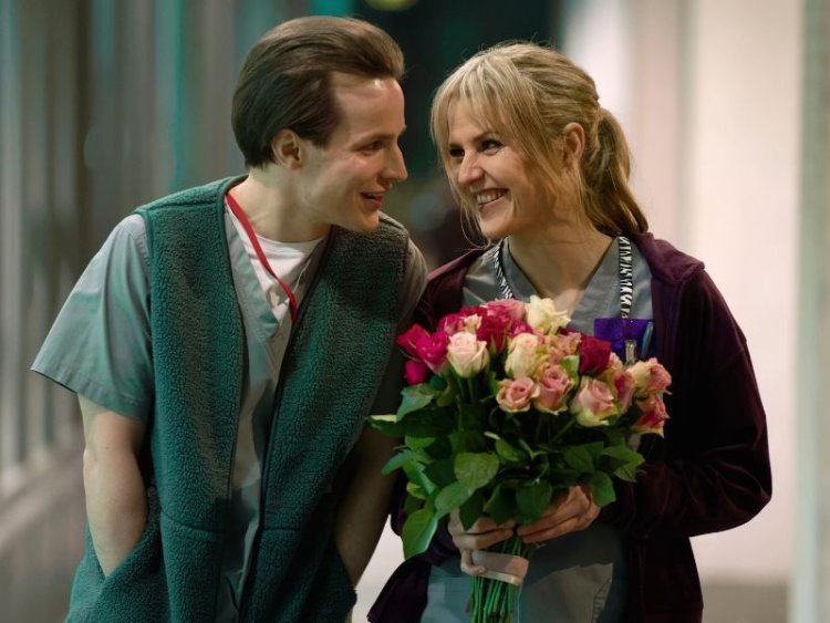 Elokuvan hahmoja puolilähikuvassa. Toisella kädessään kukkakimppu.